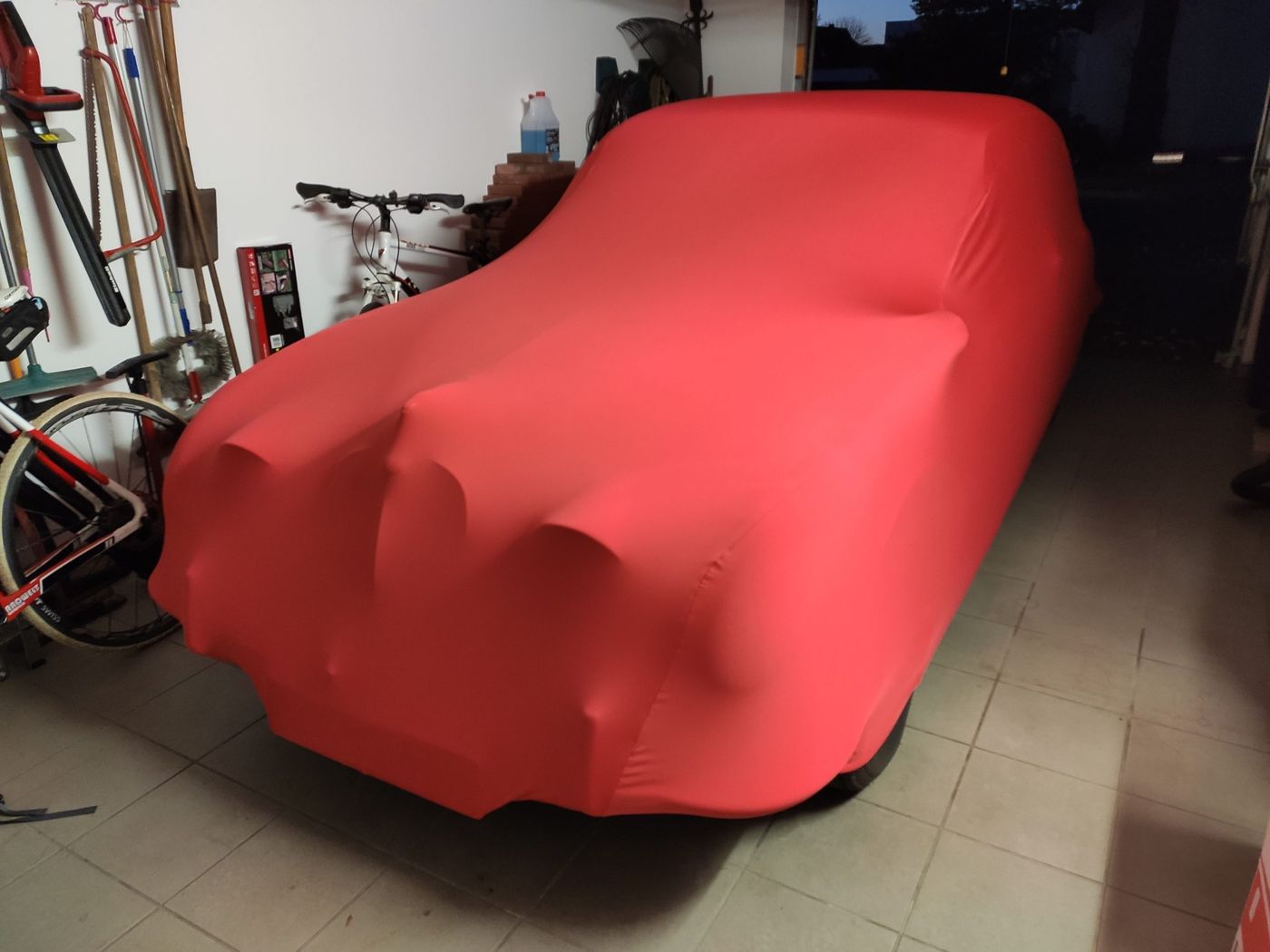 Der Jaguar unter einer roten Staubschutzdecke in der Garage
